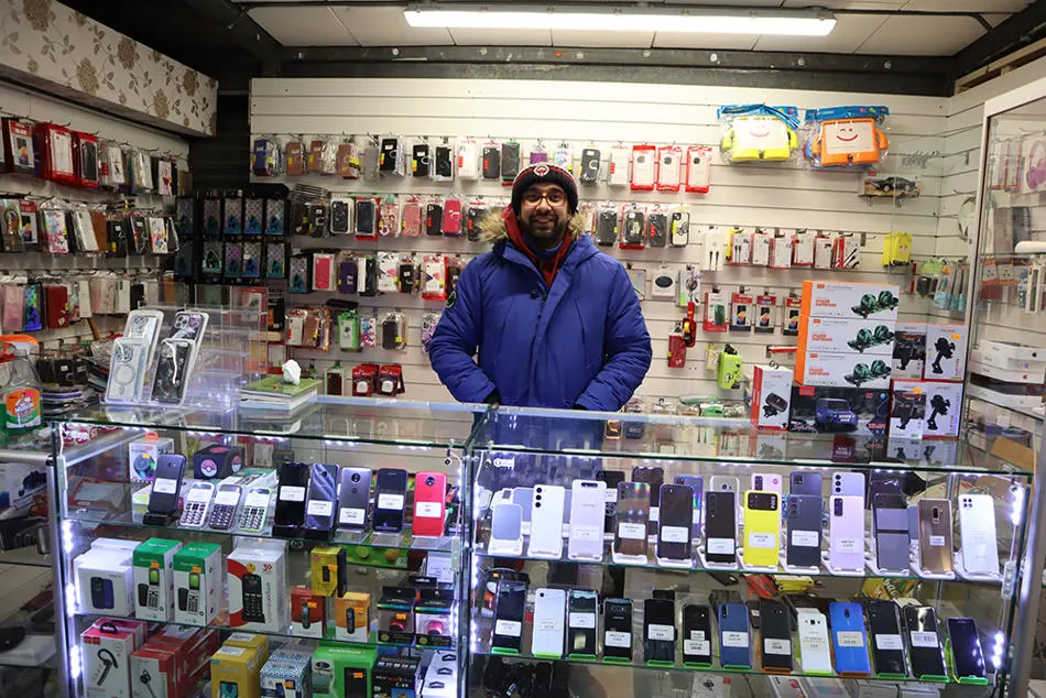 A person standing behind a counter in a shop. The walls are covered with mobile phone cases and accessories.