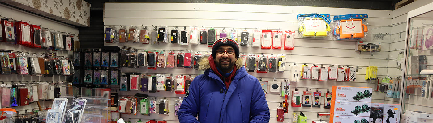 A person standing behind a counter in a shop. The walls are covered with mobile phone cases and accessories.