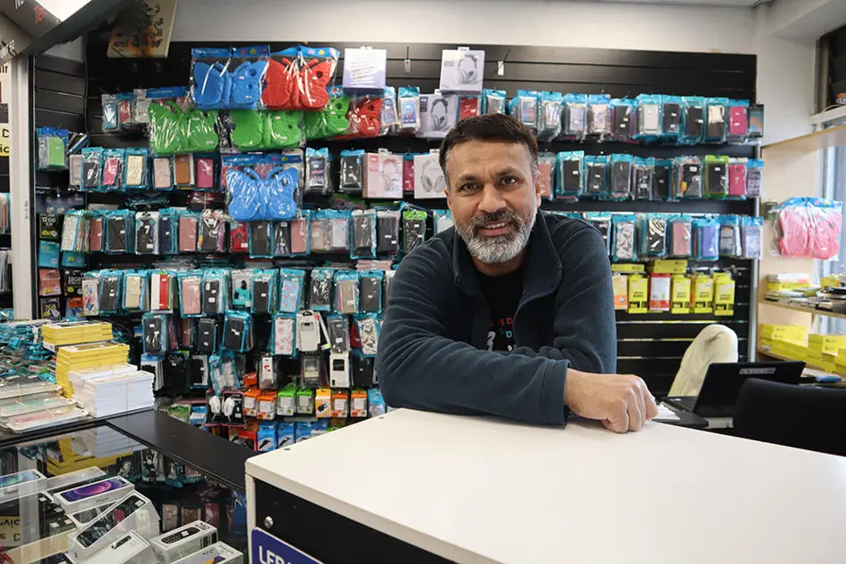 A person leaning on a shop counter in front of racks of mobile phone cases