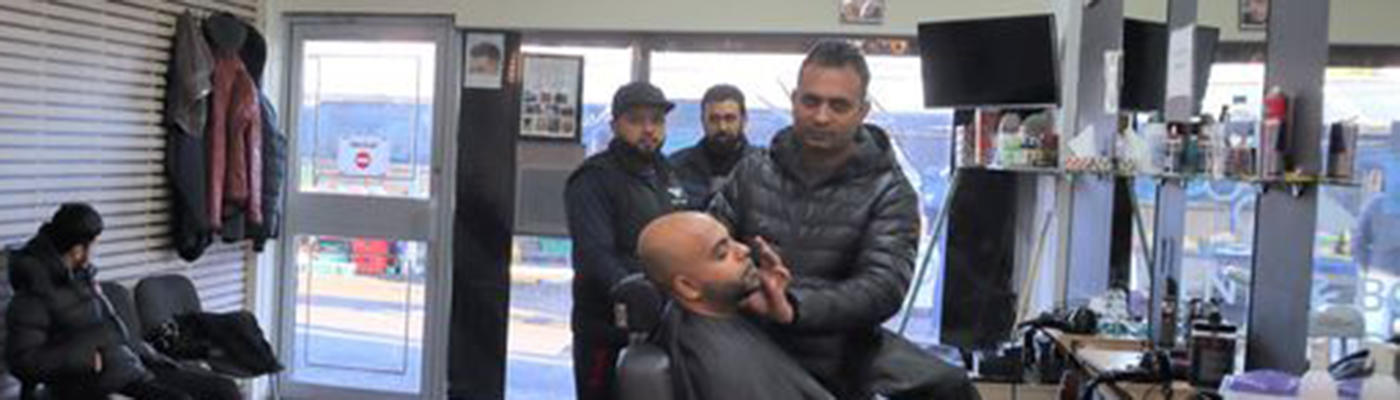 A person sat in a barber's chair with other people stood around