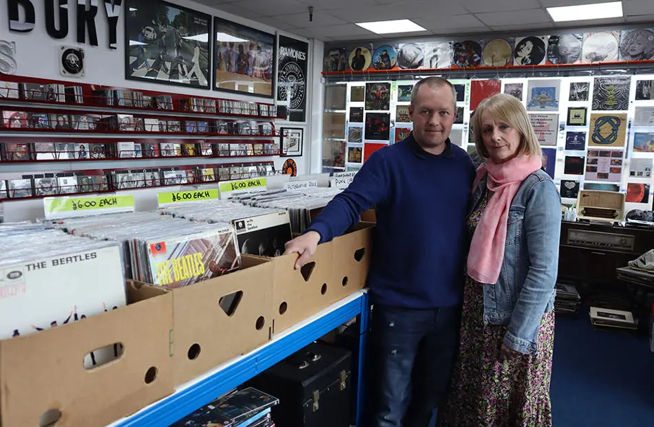 Two people stood in shop that has shelves of vinyl records and compact discs