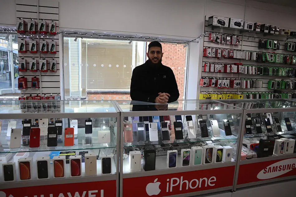 A person standing behind a shop counter with rows of mobile phones and accessories