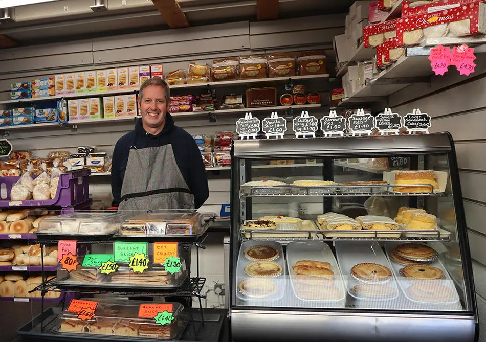 A person standing behind a counter full of cakes and pies
