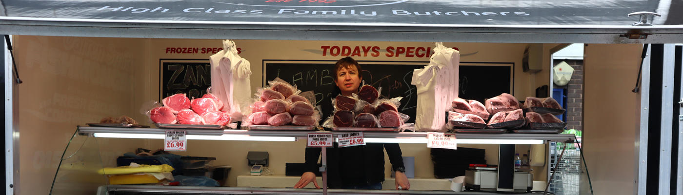 Person standing behind a glass display counter filled with cuts of meat