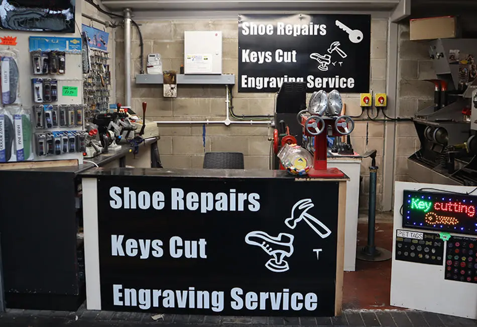 Outside market stall with shoe repair equipment. A sign saying shoe repairs, keys cut, engraving service