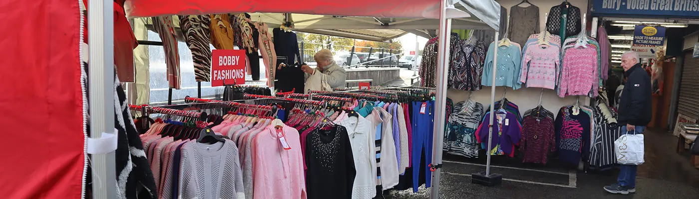 Outdoor market stalls with racks of colourful jumpers