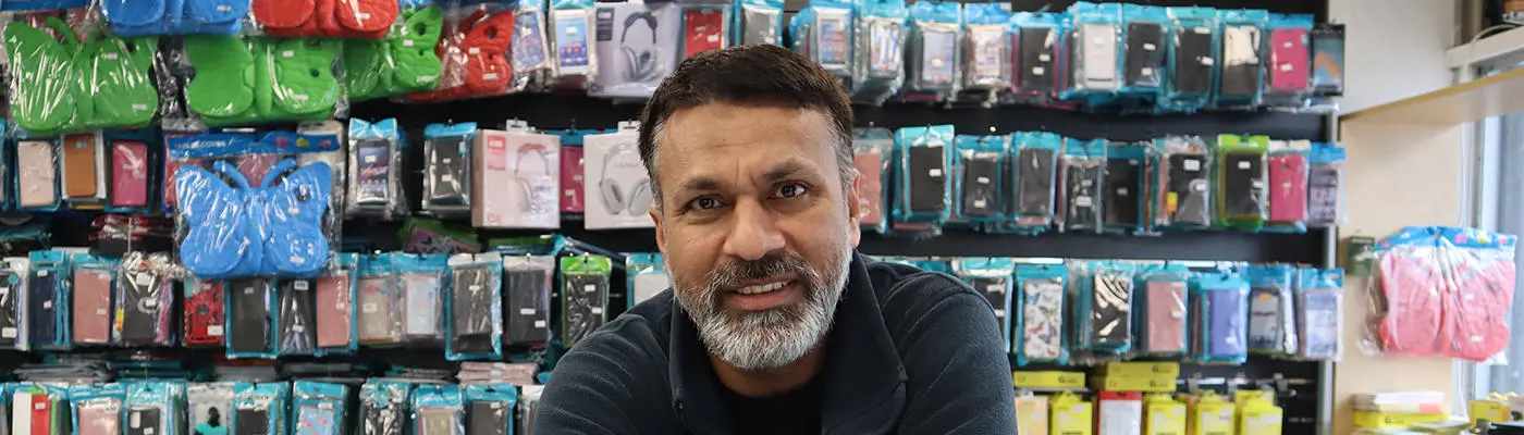 A person leaning on a shop counter in front of racks of mobile phone cases