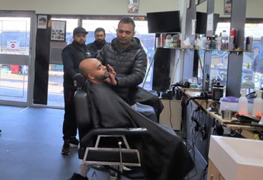 A person sat in a barber's chair with other people stood around
