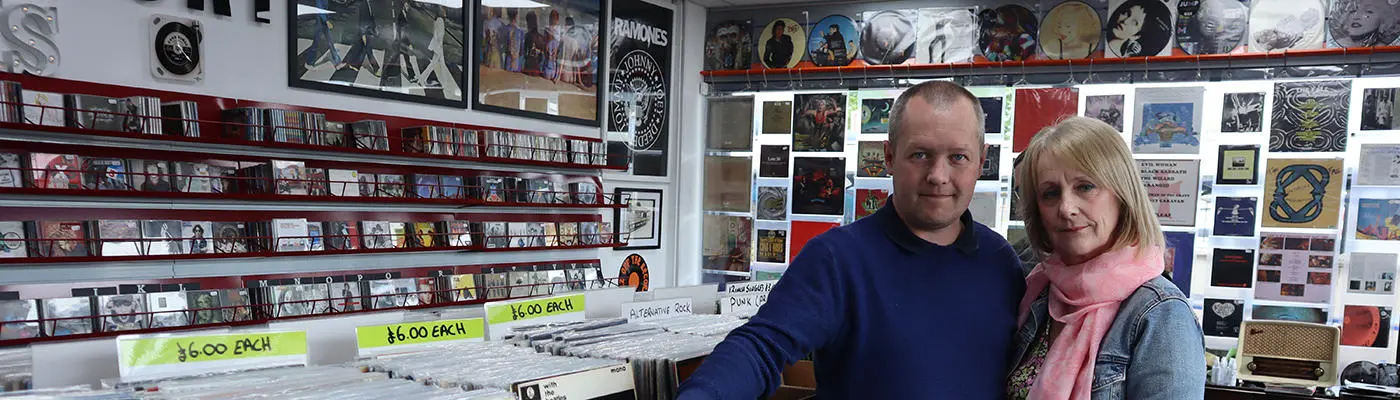 Two people stood in shop that has shelves of vinyl records and compact discs