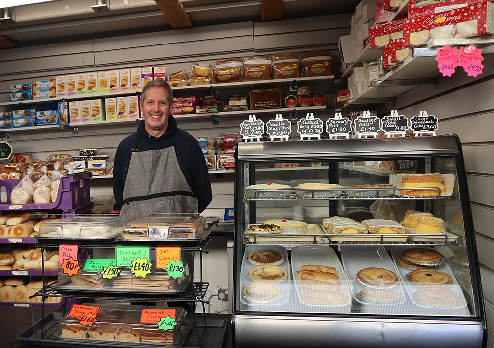 A person standing behind a counter full of cakes and pies