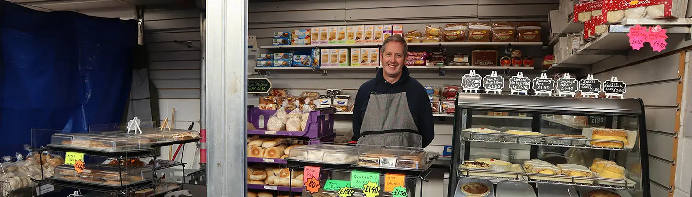 A person standing behind a counter full of cakes and pies