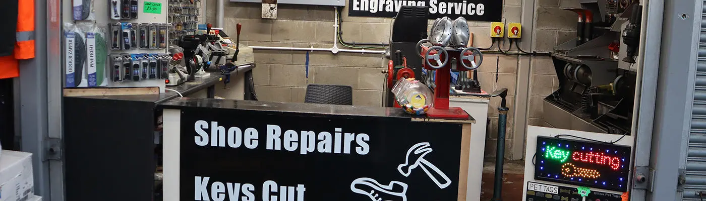 Outside market stall with shoe repair equipment. A sign saying shoe repairs, keys cut, engraving service